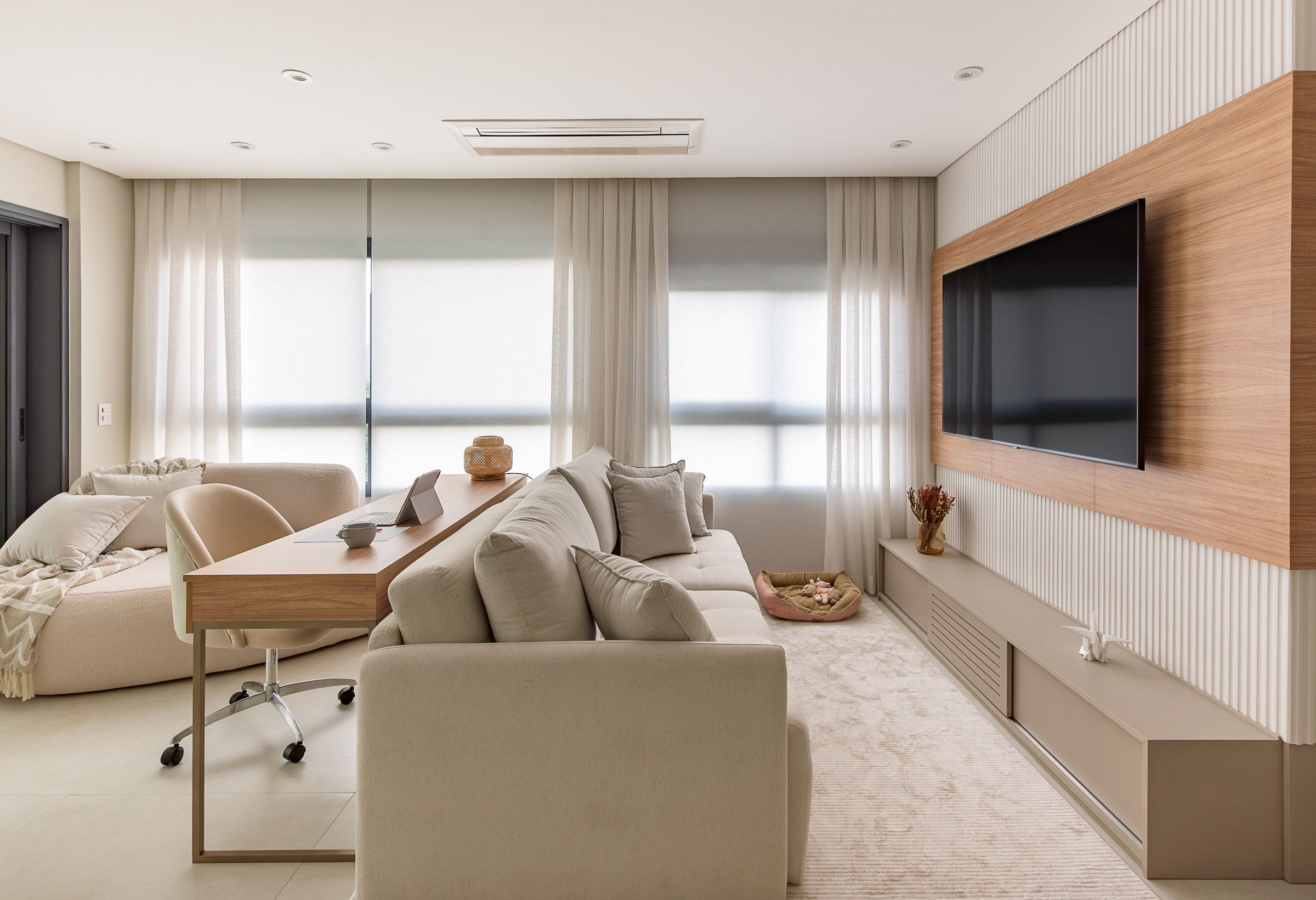 Sala de estar em tons claros, com painel ripado branco, nicho amadeirado para a TV e ar-condicionado embutido no forro