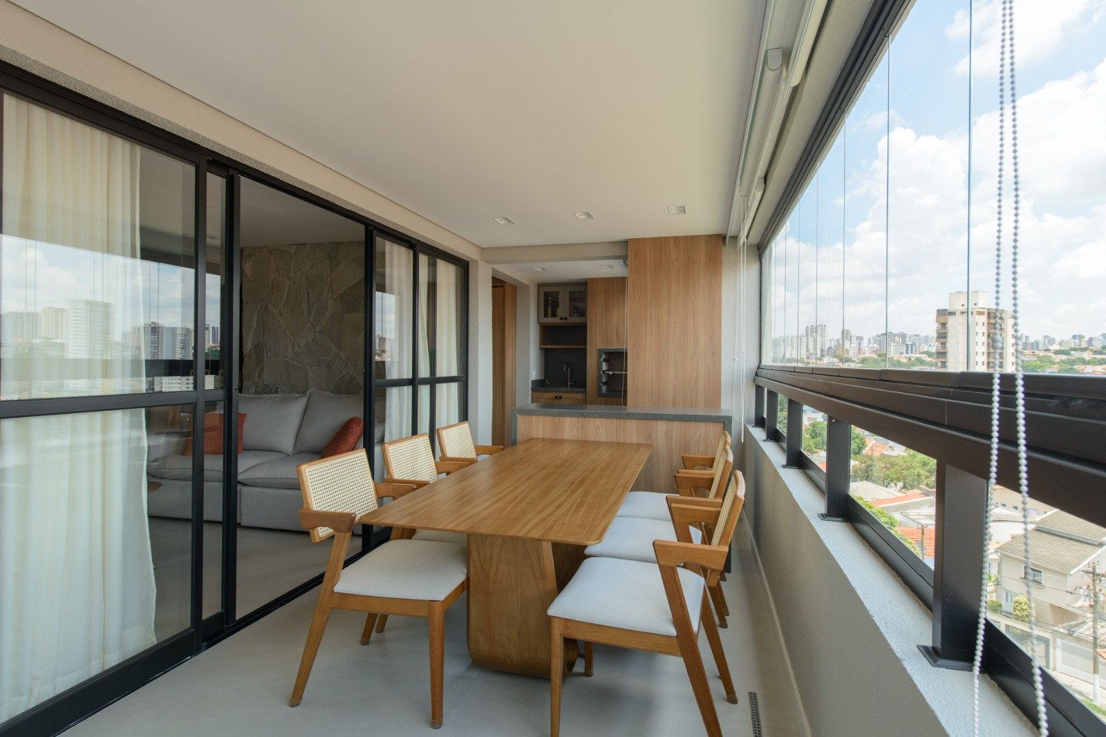 Varanda envidraçada integrada à sala, com mesa de jantar e vista da cidade